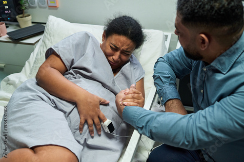Bild auf Leinwand Pregnant woman gripping partner hand while enduring labor pain in hospital bed, monitoring contractions