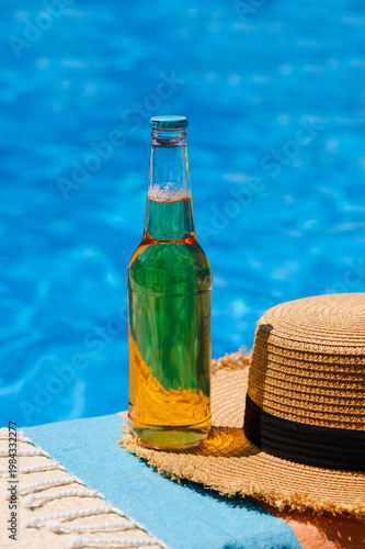 A bottle of lager and a straw hat by the pool. Summer vacation at the hotel.