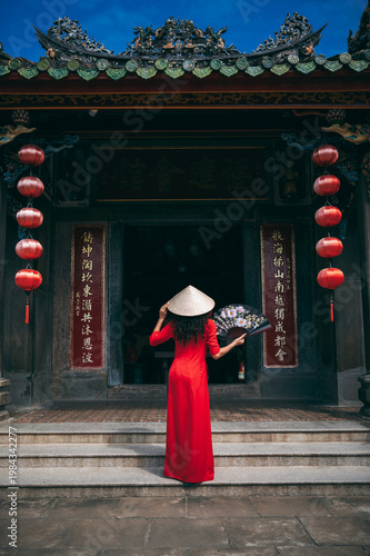 A woman in a traditional Vietnamese costume and a conical hat on the background of an ancient building in Hoi An, Vietnam.