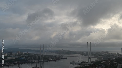 Timelapse city harbor at dusk with dramatic cloudscape and bridge silhouettes.
