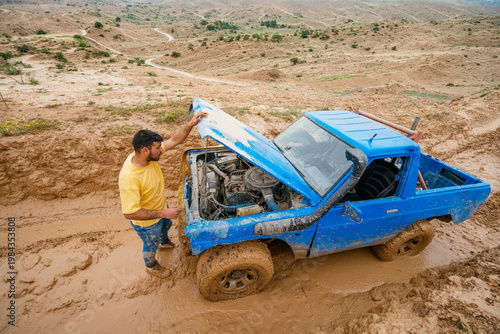 Man checking broken engine of off-road vehicle stuck in mud