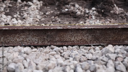 Low angle close up shows rusted railway rail on crushed ballast, yellow guideline along the top, slow pan focus shift, overcast light, shallow depth of field.