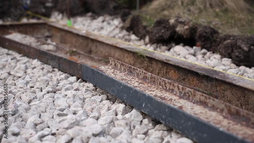 Two parallel rusted rails rest on crushed stone ballast as a taut yellow guideline runs along the outer rail. Shallow depth of field, muted tones, overcast daytime.