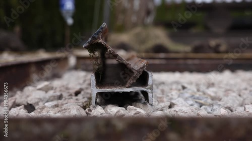 Close up steel rail sections on crushed ballast between tracks. Rust and moss cling to the top piece. Frame level view, shallow depth of field, overcast daytime.