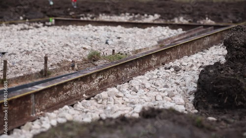 Rusty steel rails set in pale crushed stone ballast with yellow tape on tops. Slow tracking along rails under overcast light shows rust texture and recent work mood.