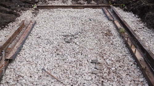 Close low angle view shows rusted rails, wooden stakes, and crushed limestone. Yellow string marks alignment, with soil edges showing fresh excavation work.