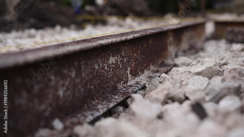 Rusted rail on pale ballast with yellow cord and lateral slide. Title appears. Close up, low angle view with shallow depth of field and muted tones conveys neglect.