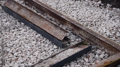 Close up captures rusted rail segments and short beams on pale ballast. Shallow depth of field isolates midplane details, with moss, flaking, and a yellow guideline.
