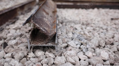 Close up low angle view of two short rail sections on coarse ballast, one bent and corroded, hollow cross section visible, soft natural light, shallow depth of field.