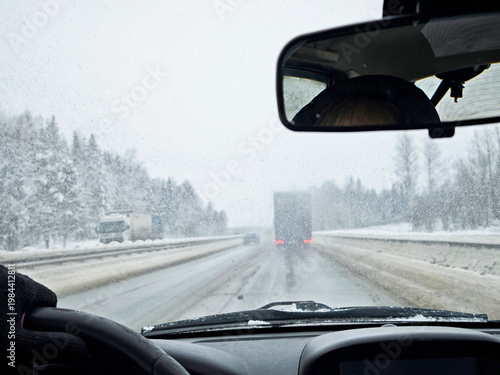 Driving through poor visibility on a winter road with a frozen and dirty windshield in a snowy landscape