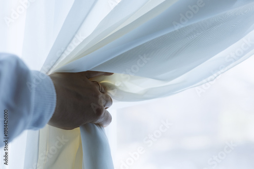 A woman moves the tulle with her hand to look out the window.