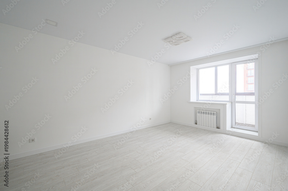 Fototapeta premium bright, minimalist room with white walls and ceiling, light wooden flooring, a large window with a radiator, and a modern ceiling light fixture. Clean, airy space, ready for furnishing