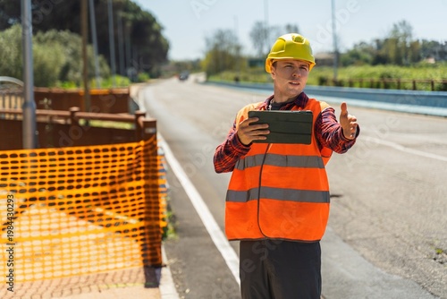 Fotografija Road engineer directing work while using tablet near construction safety barrier