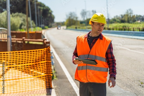 Road construction worker using tablet near safety barrier on asphalt road