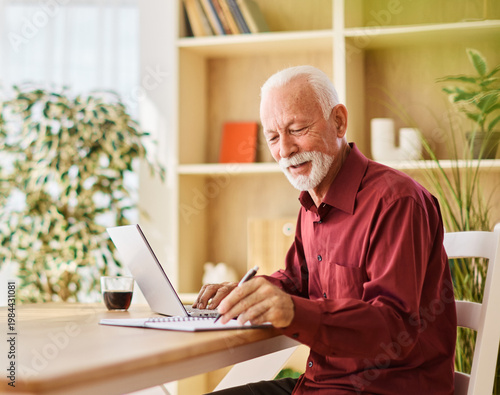 Portrait of a senior mature man or businessman having a video call on laptop in his home office at home