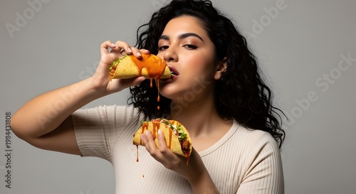 Woman enjoying tacos with sauce against a gray backdrop
