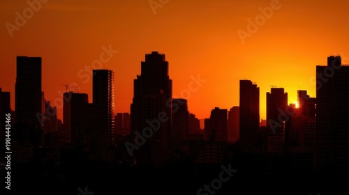 Silhouette of city skyscrapers under vibrant orange sunset sky, sun descending between buildings with serene glow.
