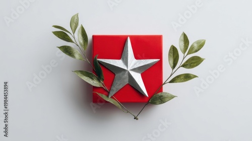 Elegant red gift box with silver star and green foliage, minimalist festive decor on white background.