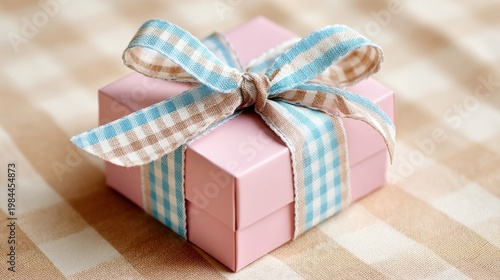 A pink square gift box with blue white and beige plaid ribbon, placed on beige plaid tablecloth, soft light.