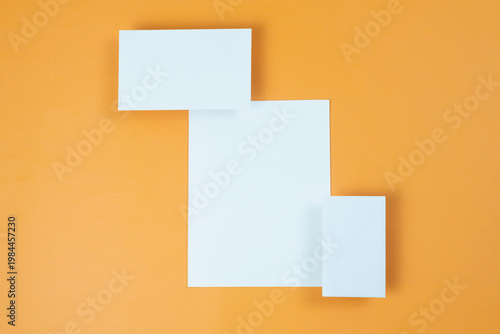 Mockup for design of white blank sheets of paper of different sizes and shapes, cards, envelope on orange background.  Creative layout