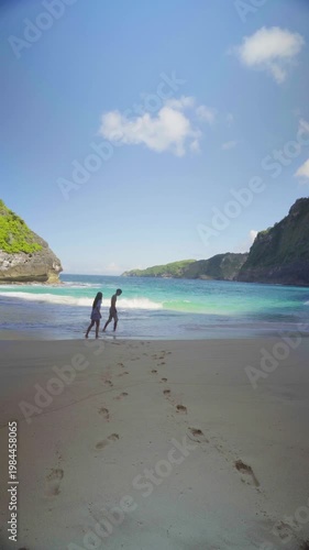 Couple standing on the beach at Kelingking on Nusa Penida, Bali, looking at ocean waves and enjoying romantic tropical scenery