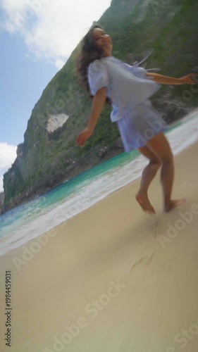 Young woman running on the beach below Kelingking cliffs on Nusa Penida, Bali, enjoying ocean waves and tropical freedom.