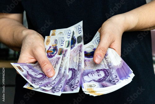 A stack of twenty pound banknotes from the Bank of England featuring Queen Elizabeth II in hands of a woman