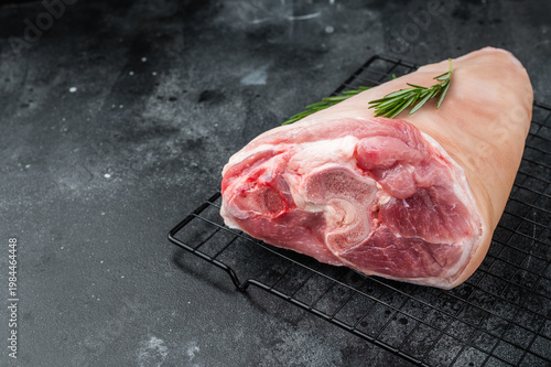 Fotografía Raw pork knuckle on cooling rack with rosemary on dark stone surface perfect for cooking guides butchery visuals and recipe content
