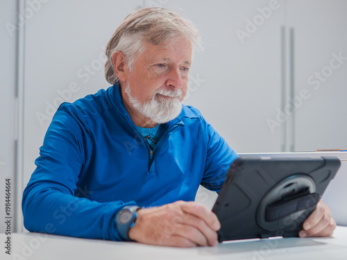 Senior man uses tablet at table in well-lit room during daytime