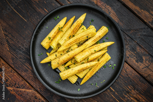 Fotografija Golden fried baby corn with thyme served on black plate rustic vegetarian dish o