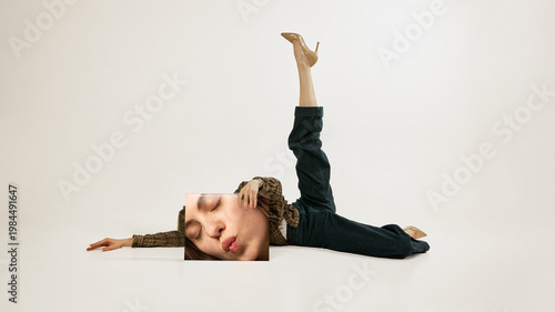 Canvas Print Young woman lying with leg raised holding printed face panel minimal fashion studio portrait