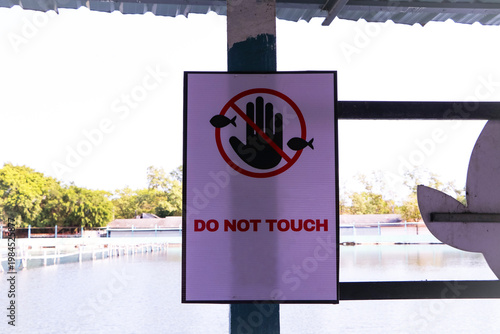 Warning sign displaying “Do Not Touch” with hand symbol placed near water area in public park. Concept of safety regulation restricted interaction, environmental protection. Ideal for themes of public