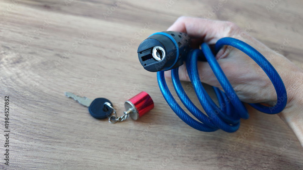 Naklejka premium Holding a blue coil lock with key in hand on wooden surface