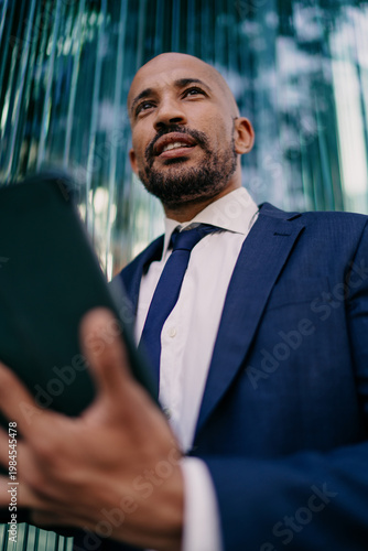 Businessman looking upward while holding tablet, portraying vision, inspiration, and future thinking in the context of digital transformation and leadership in mobile business.