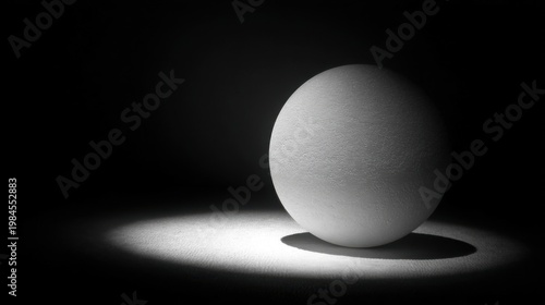 A white sphere on black background illuminated by spotlight with soft textures and sharp shadow contrasts.