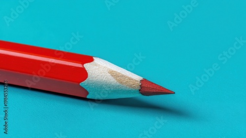 A sharp red pencil with visible wood grain rests on a teal background, showcasing its vibrant pigment core.