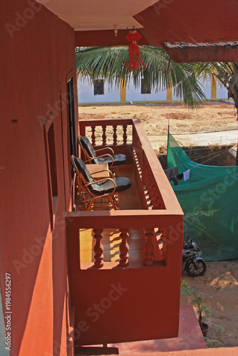The balcony of a building overlooking a sandy area and palm trees in Goa, India.