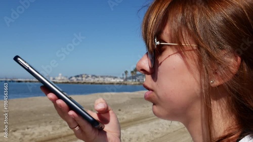 Young woman recording voice message on smartphone at the beach.