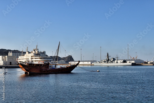 Port view from the Mutrah Fort in Muscat. Traditional boat dhow, luxury megayacht and Type 42 destroyer of Royal Navy of Oman mooded on piers. Sultanate of Oman