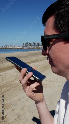 Young man recording voice message on smartphone by the sea.