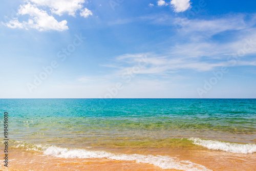 A tropical summer seascape with a sandy beach and turquoise sea. White foamy wavesBackground for vacation and cruise advertising.