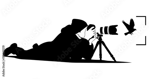 Photographer lying down with camera and tripod capturing a bird in flight