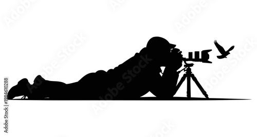 Photographer silhouette lying down with bird in flight during outdoor pursuit