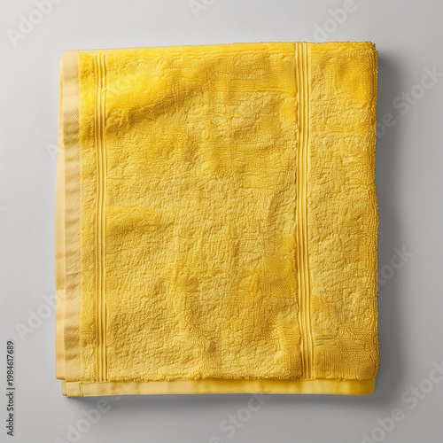A folded yellow towel placed on a light gray surface. The towel has a textured pattern and is neatly arranged, showcasing its vibrant color.