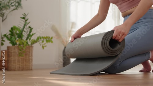 Hands of Asian woman rolling grey yoga mat after fitness class