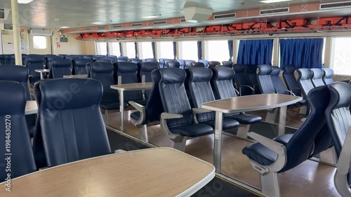Ferry interior with empty blue seats and wooden tables, showcasing modern transportation design