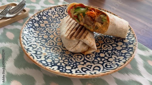 Close-up of grilled chicken wrap with vegetables on patterned blue plate, perfect for backgrounds