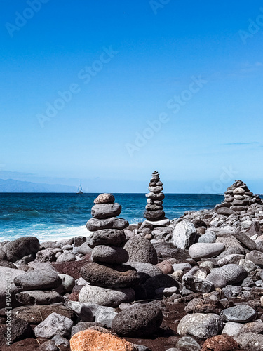 Stone cairns on volcanic beach with ocean waves, Playa del Duque Norte, Tenerife