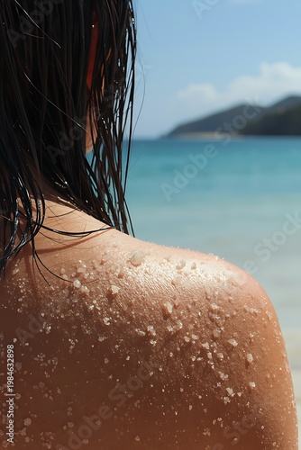 Close-up of a woman's shoulder with salt crystals on her skin at the beach with ocean view