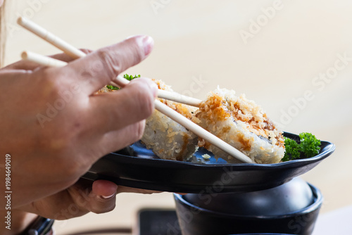 Close-up of a person using chopsticks to eat a crispy Salmon Tempura sushi roll, a vibrant and delicious Japanese lifestyle food photography.